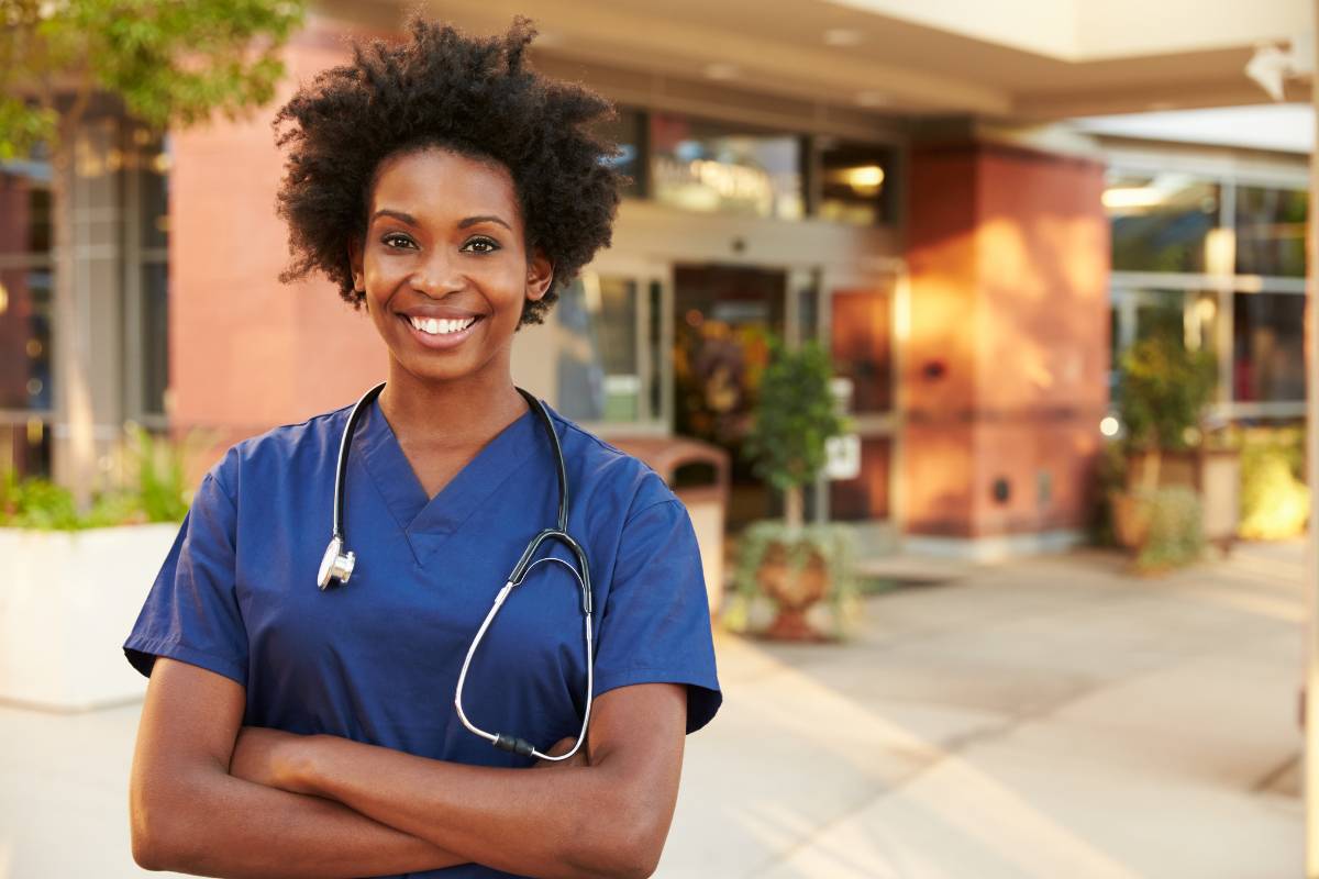 A woman in blue scrubs with a stethoscope standing outside a building