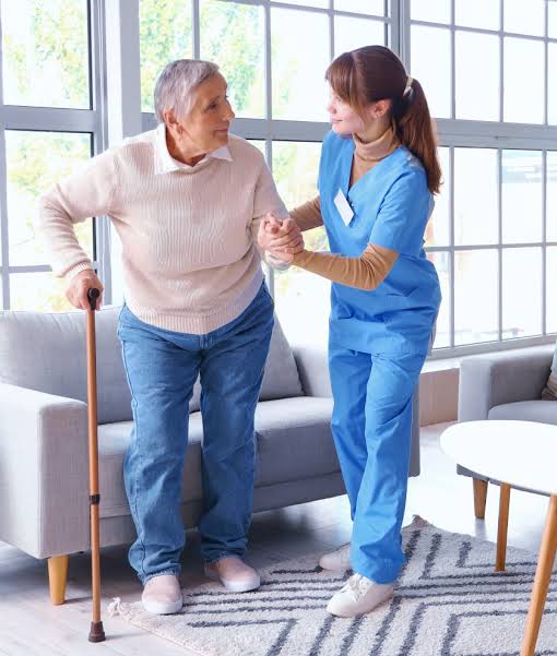 A caregiver supporting an older woman as she stands with a walking stick