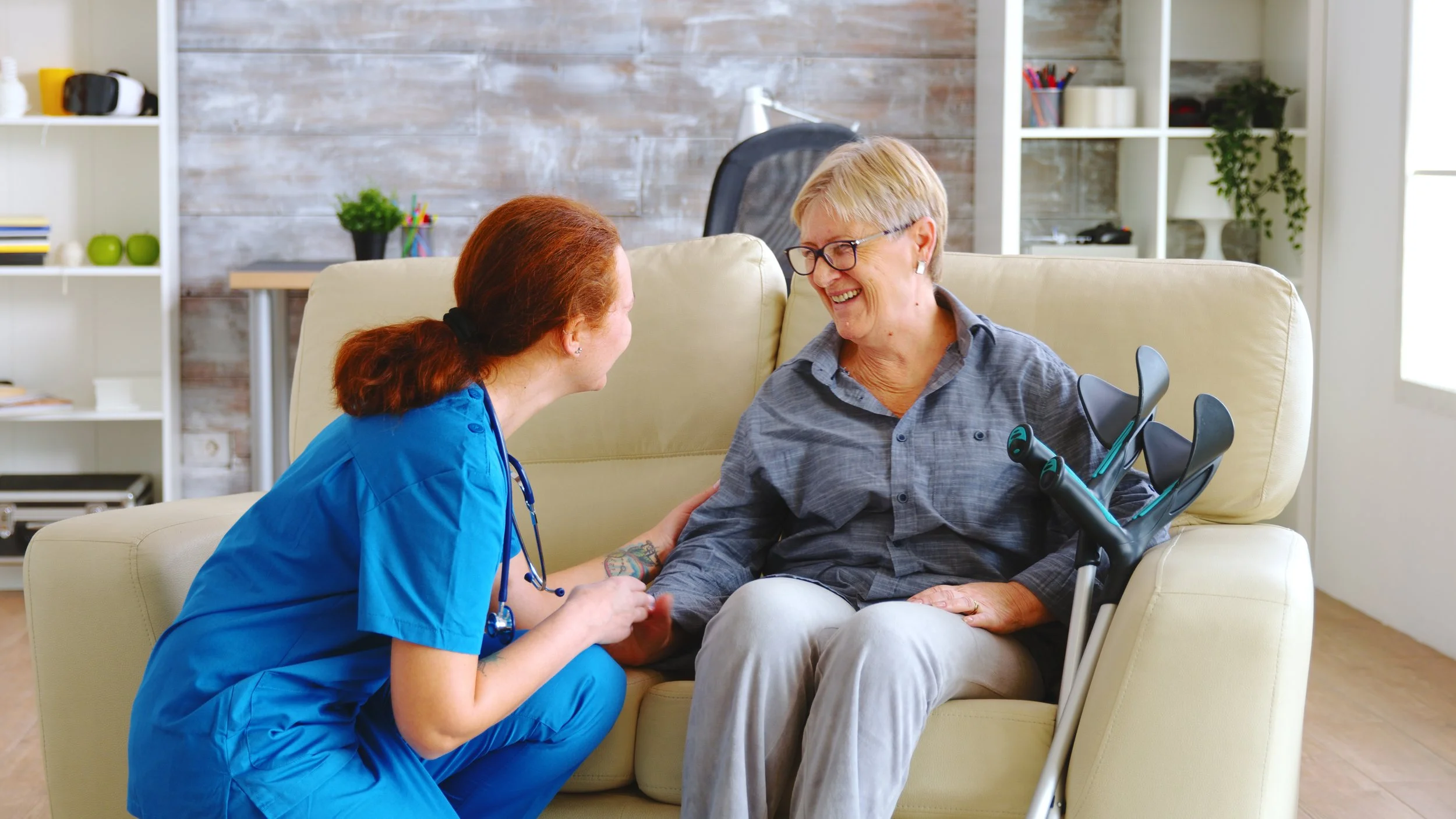 A nurse talking with an older woman seated beside her crutches at home