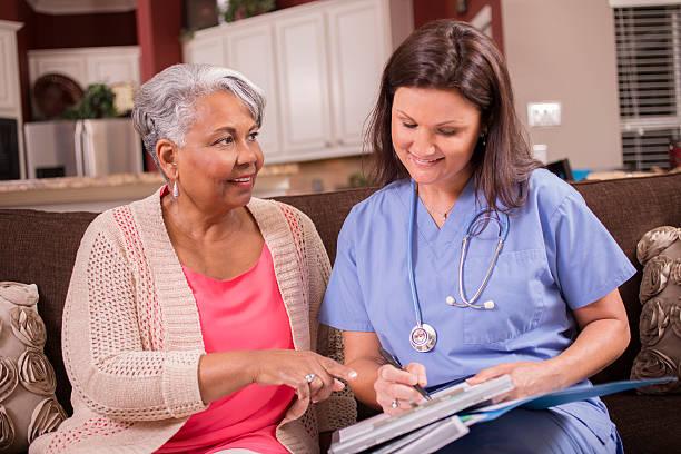 A nurse and an older woman reviewing notes together on a sofa